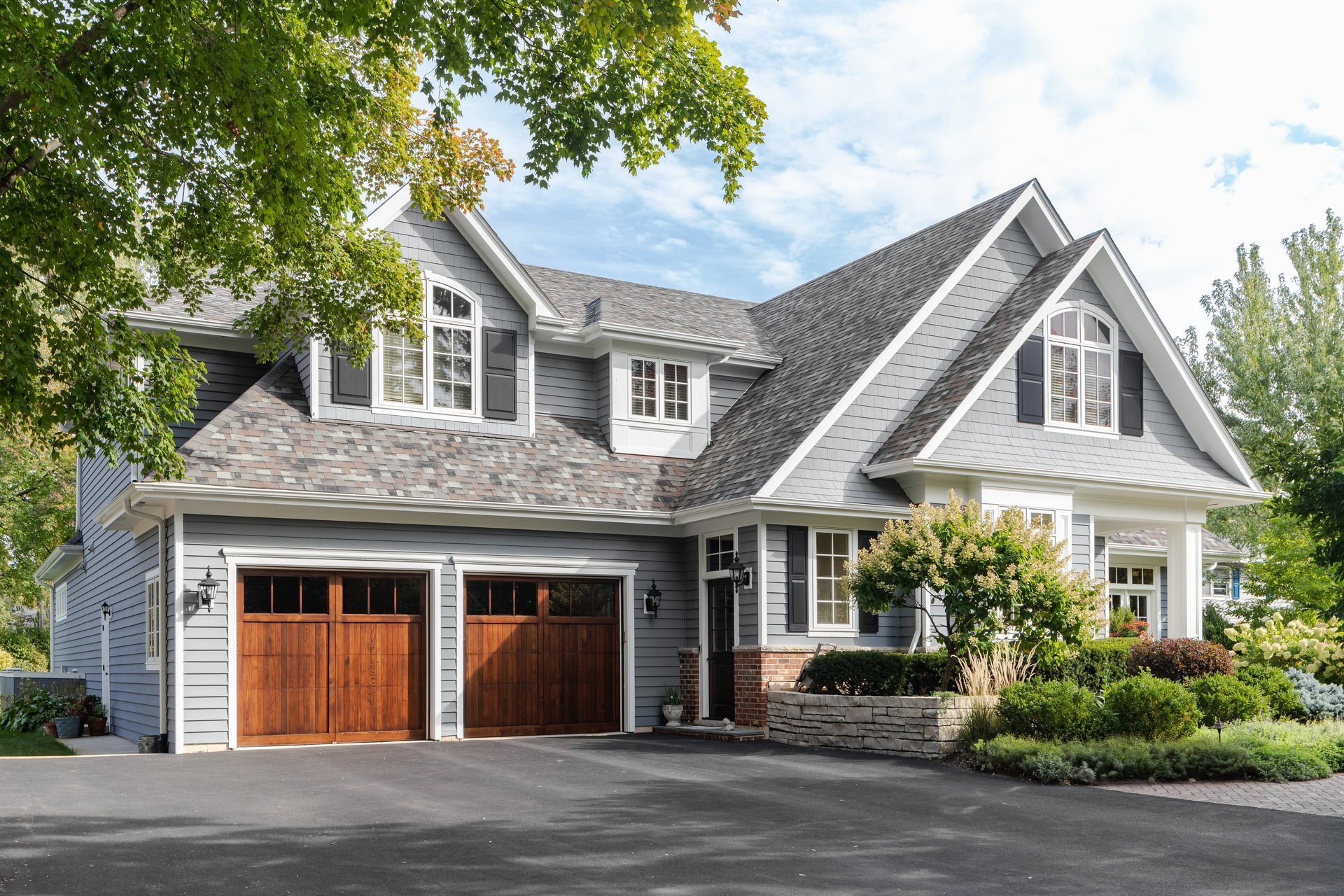 Naperville, IL, USA - A large grey and white modern farmhouse with two wooden garage doors, and beautiful landscaping