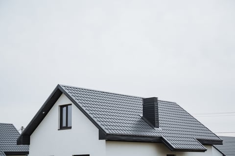 The architectural structure is a beautifully designed white house with a striking black roof and tall chimney, creating a charming and appealing appearance in its lovely surroundings