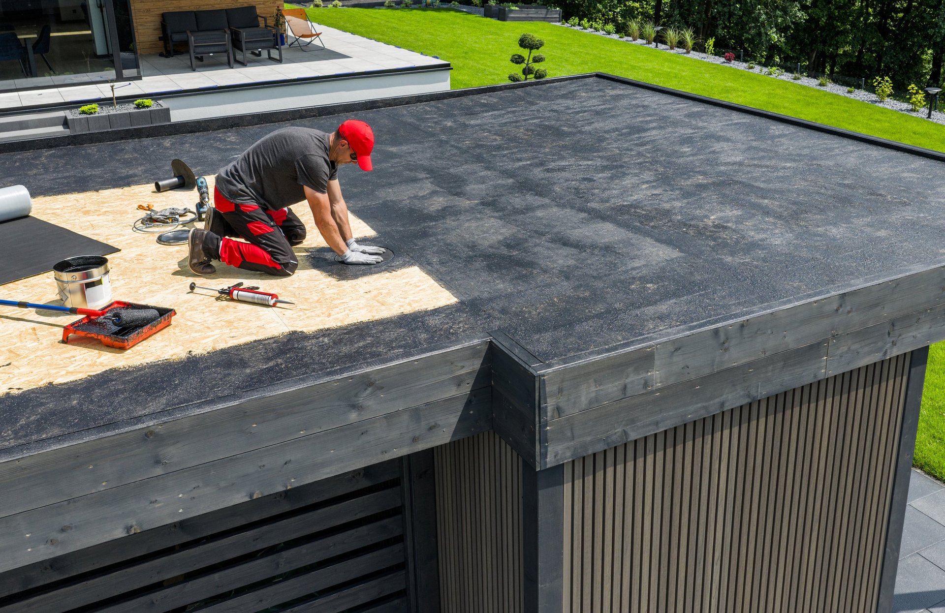 A construction worker applies EPDM roofing material on a flat roof of a modern home